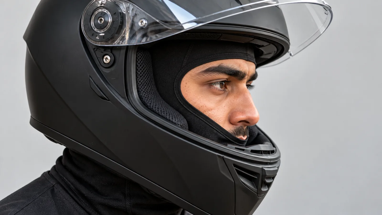 Close-up of a thin black balaclava under helmet, cheek pads of a full face helmet pressing flat against it, with the visor raised